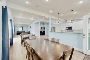 A modern kitchen with white cabinets, a central island, and a dining area with a wooden table and chairs. - Blessings on the Bay (Corpus Christi)
