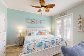 Une chambre à coucher comprenant un lit, un ventilateur de plafond, une table de chevet, une commode et une fenêtre avec des stores.