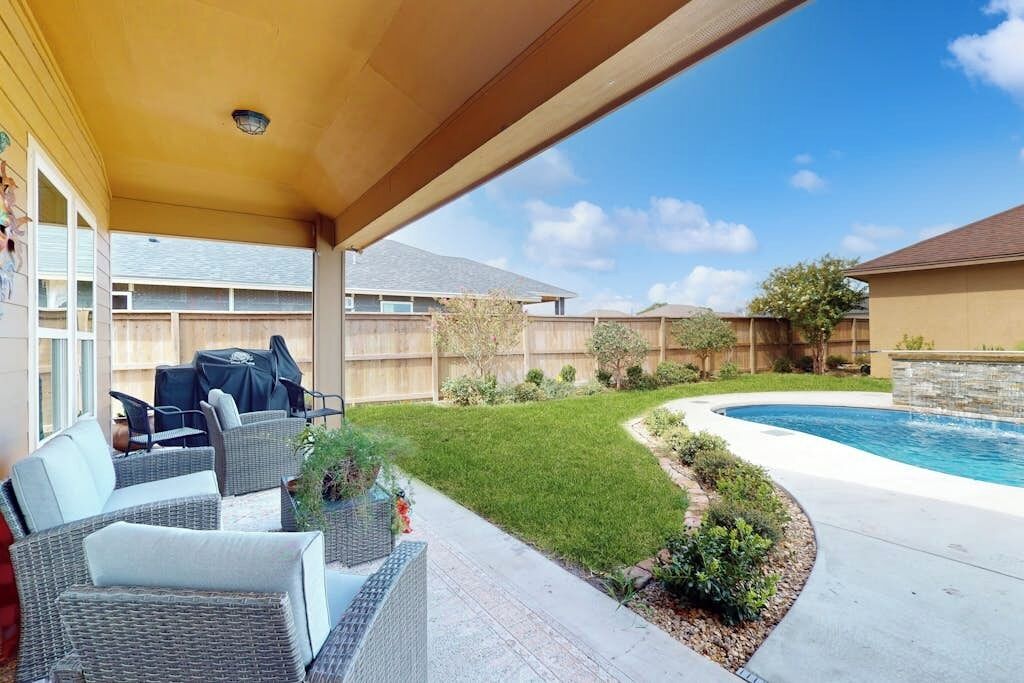 A covered patio area with outdoor furniture, a swimming pool, and a landscaped garden.