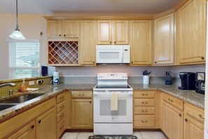 A kitchen with wooden cabinets, a white microwave, a stove, and a sink. - Take Me To The Beach (Rockport)