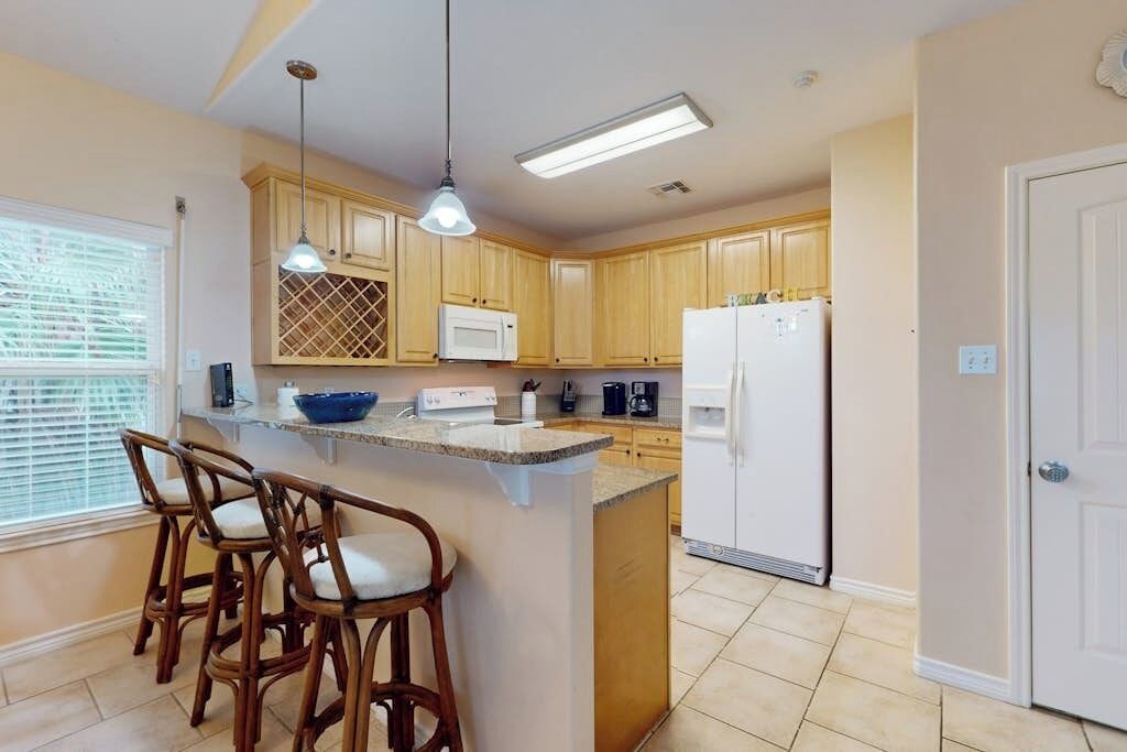 A kitchen with wooden cabinets, a white refrigerator, a microwave, and a bar stool area.