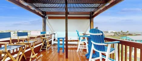 Una terraza techada al aire libre con suelo de madera, sillas Adirondack azules y blancas y una mesa.