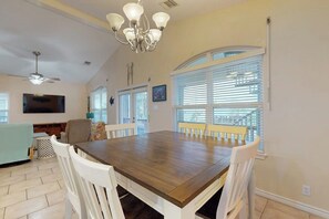 A dining area with a wooden table and white chairs, a chandelier, and a view of a balcony with a railing. - Take Me To The Beach (Rockport)
