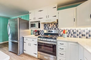 A kitchen with white cabinets, a stainless steel refrigerator, a microwave, and a stove. - Flip Flop Inn - Patio, 2 Blocks from the Bay (Rockport)