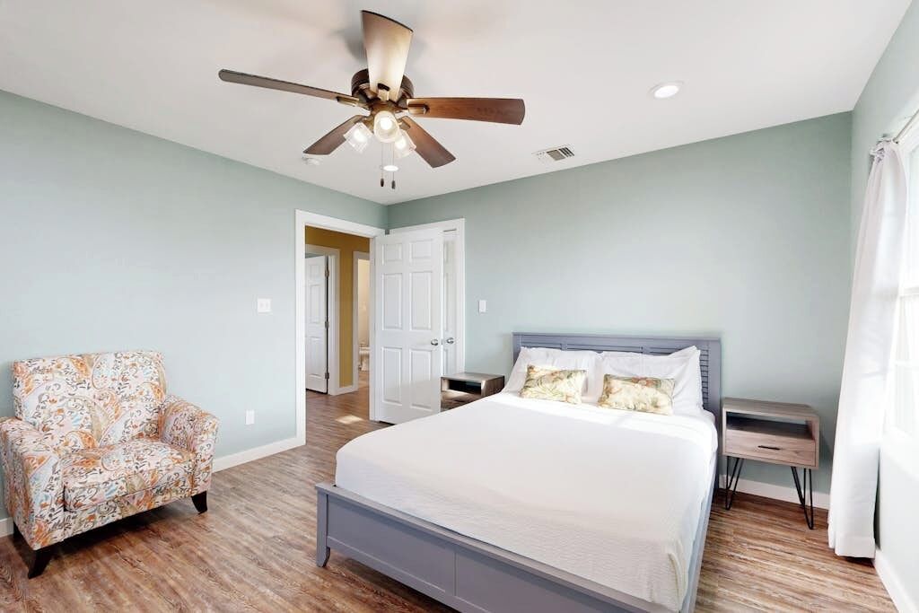 A bedroom with a bed, a chair, a nightstand, and a ceiling fan.