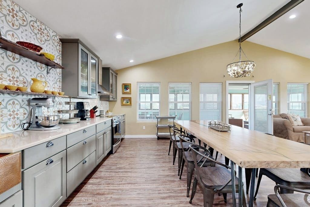 A kitchen with a long island, wooden flooring, and a chandelier.