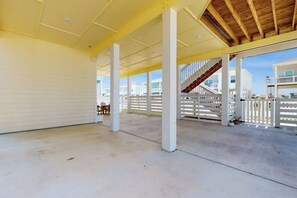 Eine offene, überdachte Terrasse mit Betonböden, weißen Geländern und einer Holztreppe, die zu einer oberen Ebene führt.