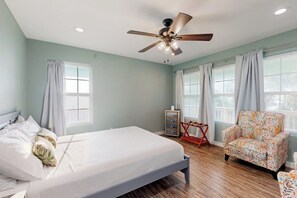 Quarto com cama, ventoinha no teto, cadeira e janela.