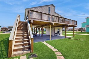 A two-story house with a covered porch and a wooden staircase leading to the upper level. - Sunset Palms - Bay Views, Pool, Close to Beach (Galveston)