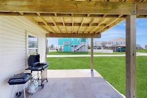 Eine überdachte Terrasse mit Grill und Propangasflasche, einem Betonboden und Blick auf die Nachbarhäuser.