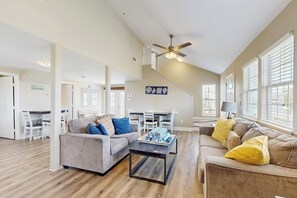A spacious living area with a ceiling fan, a dining table with chairs, and a sofa with cushions. - Sunset Palms - Bay Views, Pool, Close to Beach (Galveston)