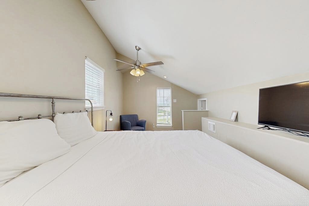 Une chambre avec un grand lit, un ventilateur de plafond, une chaise et un téléviseur.