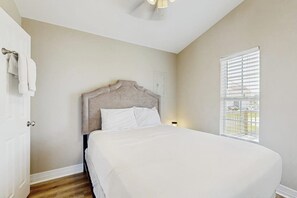 A bedroom with a bed, a door, a window with blinds, and a ceiling fan. - Sunset Palms - Bay Views, Pool, Close to Beach (Galveston)