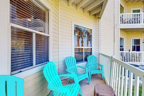 A porch with two chairs and a small table, a window with blinds, and a balcony with a railing. - Beach Club 172 - Balcony & Pool, Close to Beach (Corpus Christi)