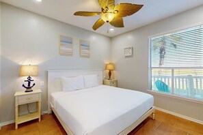 A bedroom with a bed, two bedside tables, a ceiling fan, and a window with blinds. - Beach Club 172 - Balcony & Pool, Close to Beach (Corpus Christi)