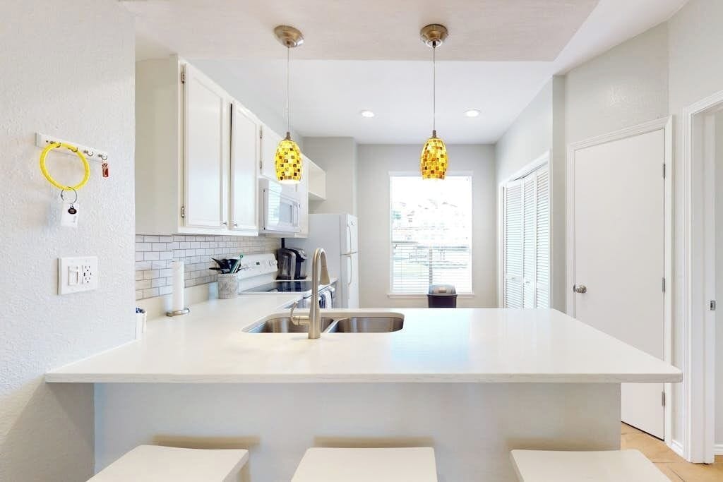 A modern kitchen with a central island, white cabinetry, and pendant lighting.