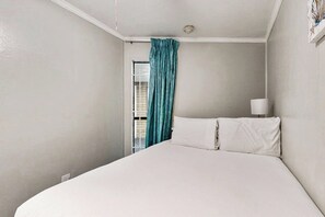 A hotel room with a bed, a window with curtains, and a wall-mounted lamp. - Casa Del Mar - Mi Casa 113 (Galveston)