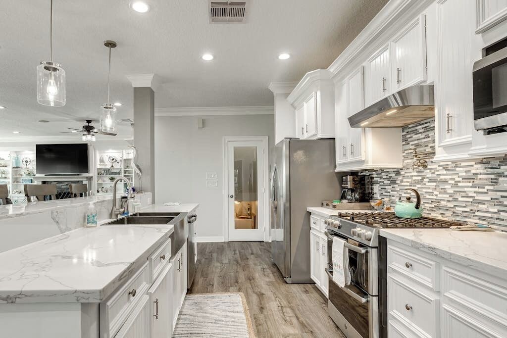 A modern kitchen with white cabinetry, a marble island, stainless steel appliances, and pendant lighting.