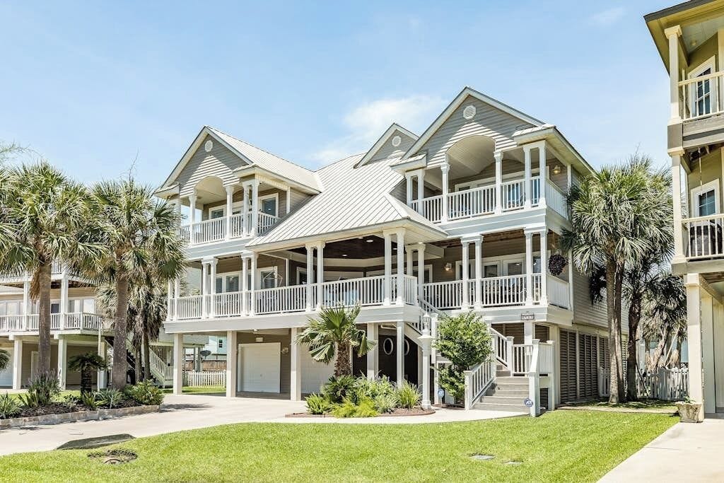 A multi-story residential building with balconies, a covered front porch, and a well-maintained lawn.