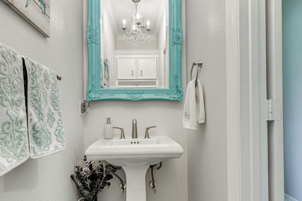Een badkamer met een wit wastafelmeubel, een spiegel met een turquoise lijst en een kroonluchter.