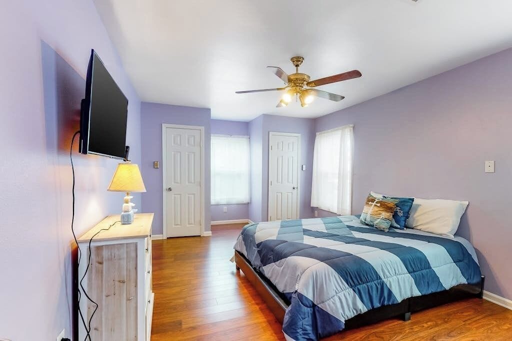 A bedroom with a bed, a ceiling fan, a TV mounted on the wall, and a lamp on a bedside table.