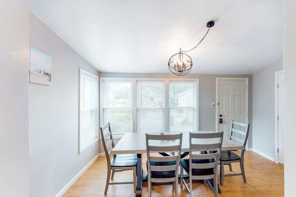 A dining area with a table and chairs, a chandelier, and a view through large windows.