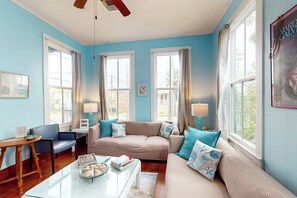 A living room with a beige sofa, blue cushions, a glass coffee table, and a side table with a lamp. - Galveston Getaway - Historic Home Near the Beach (Galveston)