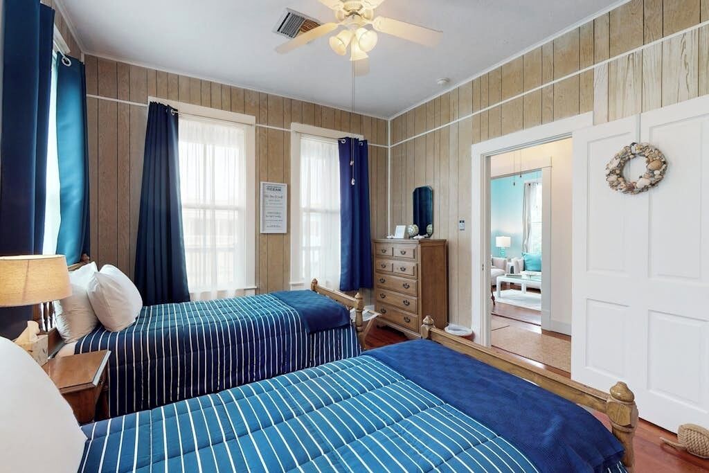 A bedroom with two beds, a dresser, and a door leading to another room.