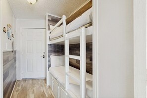 Une pièce avec un lit superposé, une porte blanche et un plancher en bois.