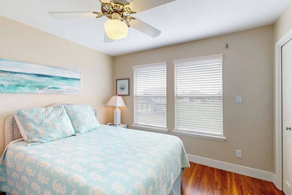 A bedroom with a bed, a ceiling fan, and two windows with blinds.
