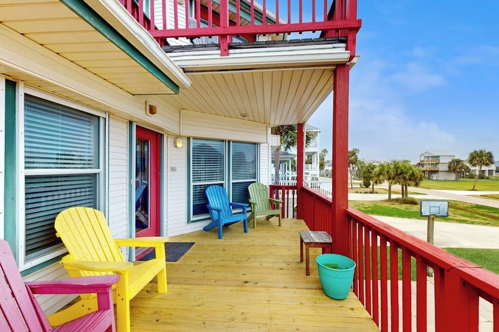 A wooden deck with colorful Adirondack chairs, a small table, and a trash bin.