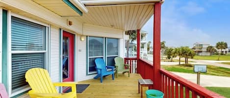 A wooden deck with colorful Adirondack chairs, a small table, and a trash bin.