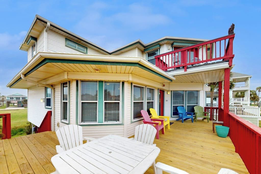 A two-story house with a wooden deck, multiple windows, and outdoor seating.