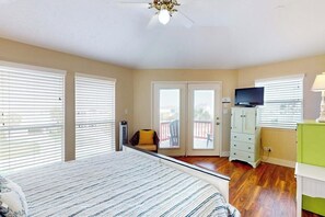 Een slaapkamer met een bed, een televisie, een dressoir en een balkon met een stoel.
