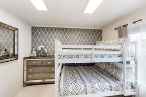 A bunk bed with patterned bedding, a dresser with drawers, a mirror, and a patterned wall. - The Waves: unit B - Modern, Close to the Beach (South Padre Island)