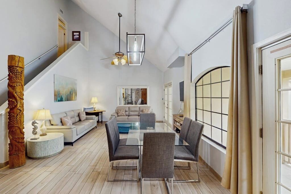 A spacious living area with a dining table, sofas, and a staircase leading to an upper level.