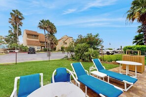 A patio with lounge chairs and a table, surrounded by palm trees and a fence. - La Solana Condominiums # 130 (South Padre Island)