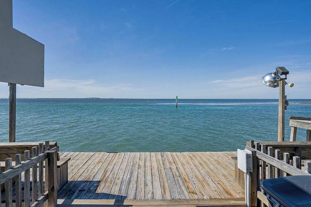 A wooden deck with a view of the sea, a metal structure on the right, and a blank sign on the left.