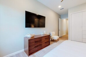 Un dormitorio moderno con una cama grande, un aparador de madera, una silla blanca y un televisor de pantalla plana montado en la pared.