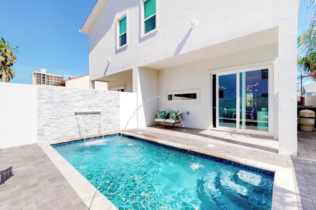 A modern house with a swimming pool, a patio with outdoor furniture, and a large sliding glass door.