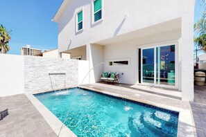 Ein modernes Haus mit Swimmingpool, einer Terrasse mit Gartenmöbeln und einer großen Glasschiebetür.