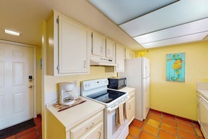 A compact kitchen with white cabinets, a stove, a microwave, and a refrigerator. - Continental #105 - Gulf-Front Condo, Beach Access (South Padre Island)