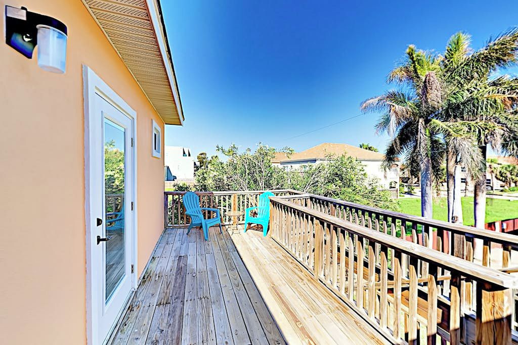A wooden deck with outdoor seating and a view of a residential area with palm trees.