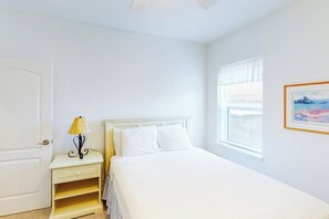 A bedroom with a bed, a bedside table with a lamp, a window with blinds, and a door. - Acapulco Townhouse - Walk to Beach & Dog-Friendly (South Padre Island)