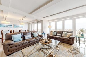 A spacious living room with two leather sofas, a glass coffee table, and large windows offering a view. - Solare Tower 705 - Gulf-Front, Ocean Views & Pool (South Padre Island)