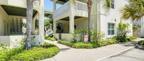 A multi-story residential building with balconies, a covered walkway, and a parking area.