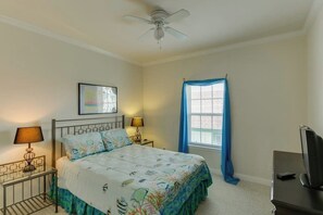 A bedroom with a bed, two bedside lamps, a ceiling fan, a window with curtains, and a television on a stand. - Cloud Dancer Condominiums 4 (South Padre Island)