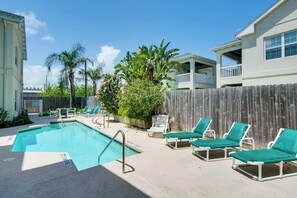 A swimming pool with lounge chairs, surrounded by a wooden fence and palm trees. - Cloud Dancer Condominiums 4 (South Padre Island)