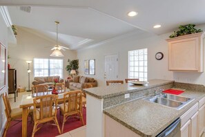 A spacious kitchen with granite countertops, a dining area with wicker chairs, and a large island with a sink. - Cloud Dancer Condominiums 4 (South Padre Island)