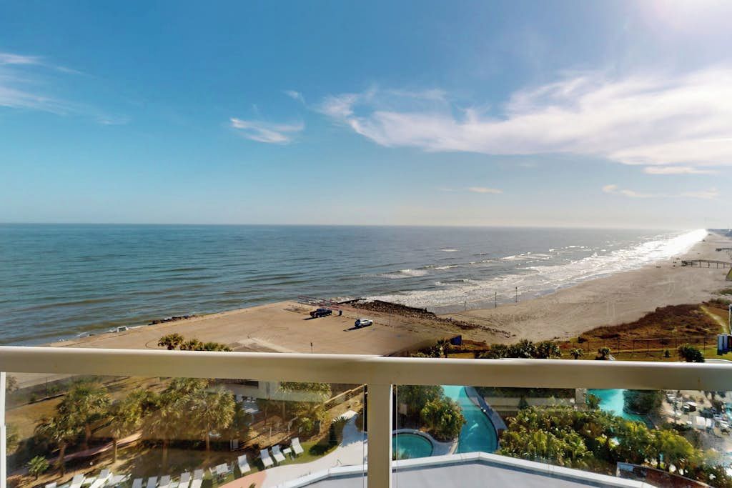 Vue sur la plage depuis un balcon donnant sur une piscine et un espace de détente.